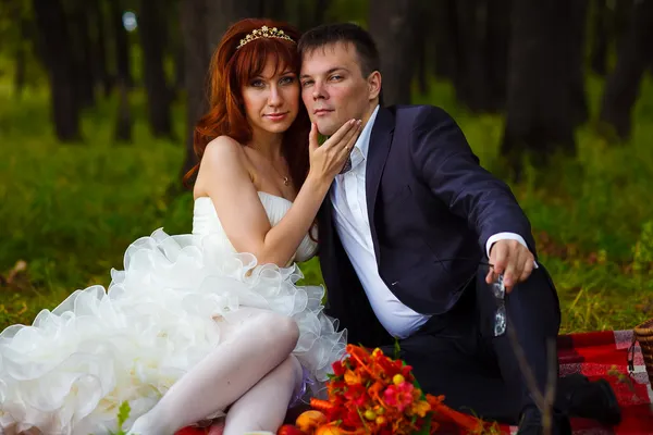 Pareja novia y novio sentado en la hierba verde, un picnic en el bosque — Foto de Stock