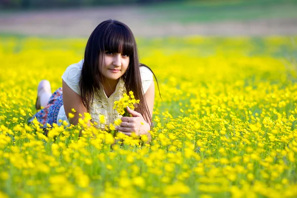 Beautiful brunette girl lying in a field of yellow flowers — Stock Photo, Image