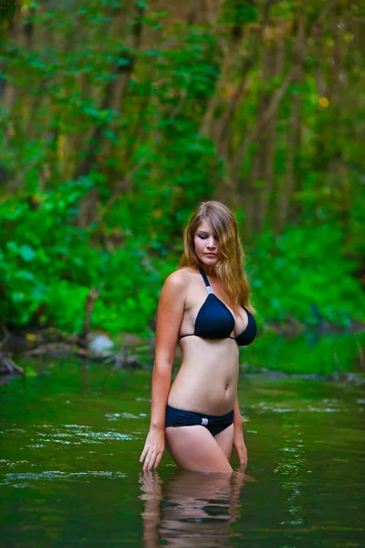 Blonde nude young woman big breasts in a black bikini standing o