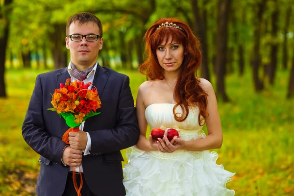Bride and groom standing on a green background in forest, red ha — Stock Photo, Image