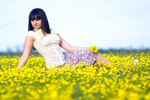 Brunette beautiful girl lying in a field of yellow flowers — Stock Photo, Image