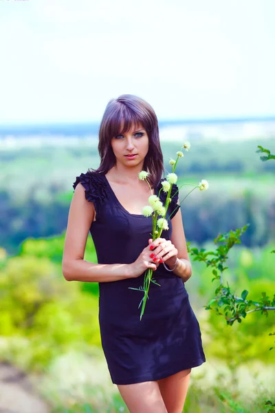 Brünette dünne Frau mit Blumen auf dem grünen Feld backgrou — Stockfoto