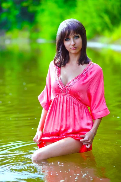 Brunette woman model in red dress wet to the waist in the water — Stock Photo, Image