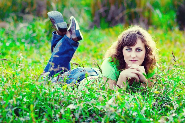 Kudrnaté vlasy girl žena v džíny a tričko, které leží na zelené trávě — Stock fotografie
