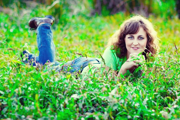 Kręcone włosy dziewczyna kobieta w dżinsy i koszulka leżącego na zielonej trawie — Zdjęcie stockowe