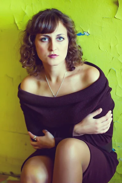 Curly girl woman in a brown dress sits near the old green wall — Stock Photo, Image