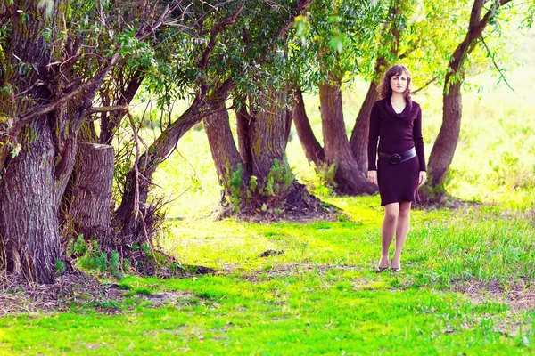 Mulher menina em vestido marrom vai para a natureza verde em torno de árvores sagacidade — Fotografia de Stock