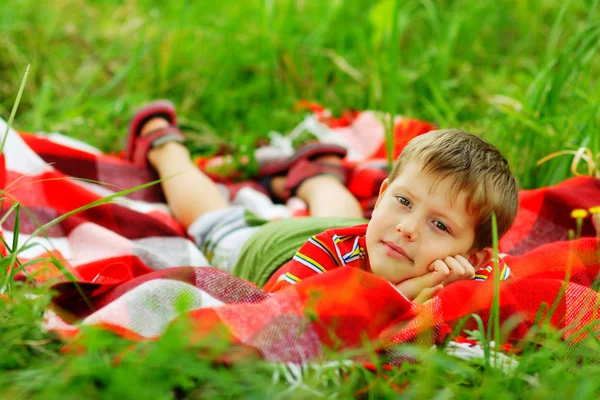 Young man in a red shirt lying in the grass on plaid — Stock Photo, Image