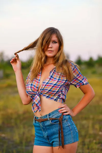 Young woman in a plaid shirt, denim shorts at sunset, flowing ha — Stock Photo, Image