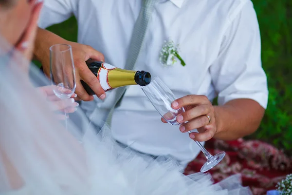 Noivo derrama vinho em um copo no casamento em um piquenique em um fo verde — Fotografia de Stock