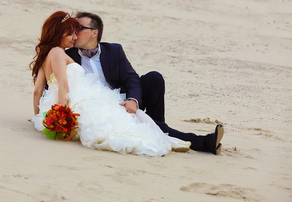 Frisch verheiratete Paare am Strand, Braut sitzt und Bräutigam küsst — Stockfoto