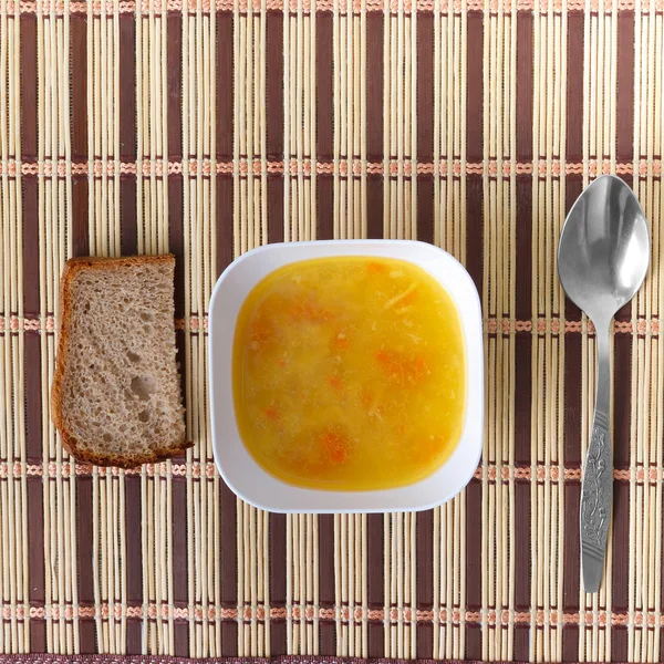 Tazón de sopa con una cuchara y pan en la estera — Foto de Stock