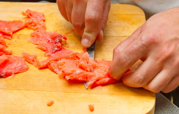 Cook cuts raw pieces of meat on a cutting board with a knife