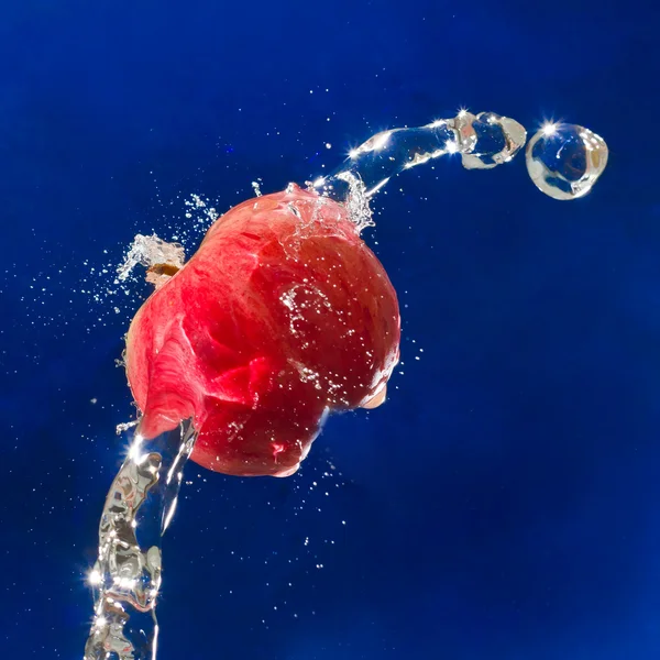 Faller rött äpple i en spray av bubblor i blå konsistens — Stockfoto