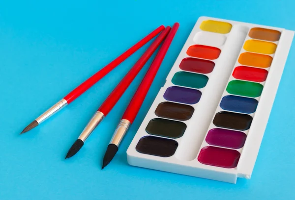 Brushes watercolour paints children on blue background — Stock Photo, Image