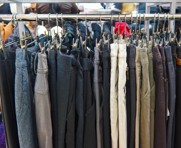 Skupina různé barevné džíny visí na věšáku v úložišti — Stock fotografie