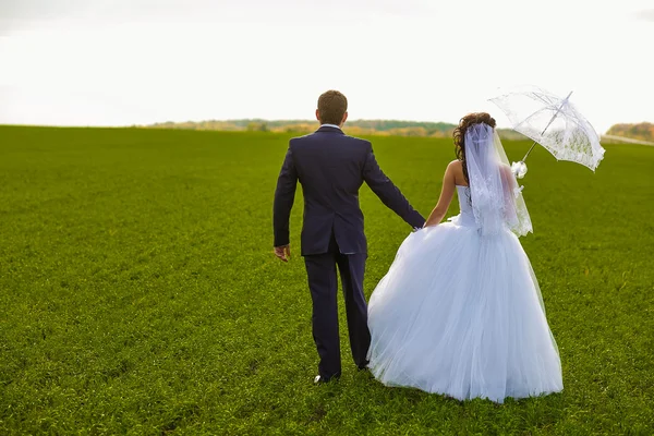 Bruden och brudgummen utomhus stående på ett grönt fält kram, nygifta — Stockfoto