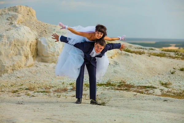 Bride and groom sitting on a white rock and playing hand in hand — Stock Photo, Image