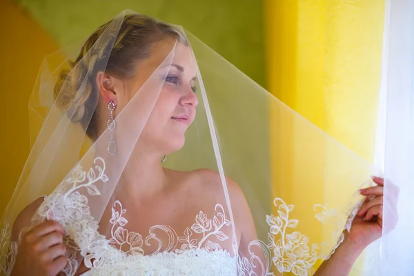 Portret sluier bruid blonde vrouw staat en kijkt uit raam lar — Stockfoto