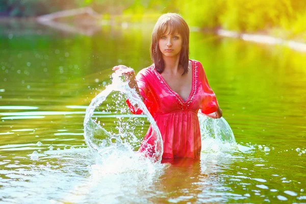 Sunlight brunette woman red dress is wet to waist in splash wate — Stock Photo, Image