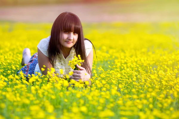 Luce del sole bella ragazza bruna sdraiata in un campo di flusso giallo — Foto Stock