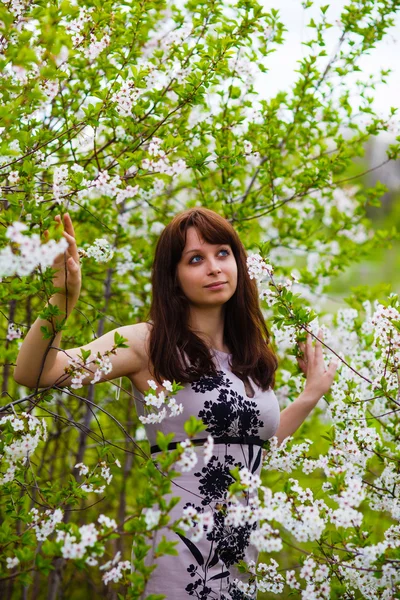 Brunette girl standing on nature looking to side around blooming — Stock Photo, Image