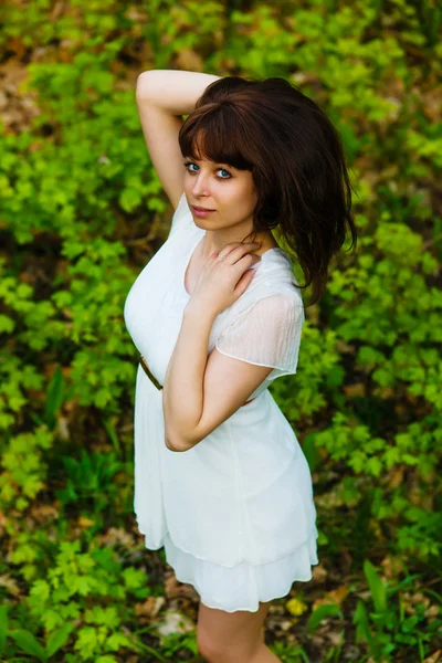 Brunett tjej rätar hår i en vit klänning som står på gree — Stockfoto