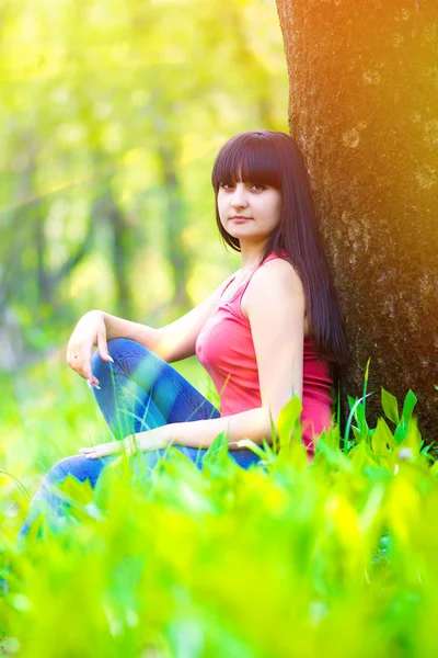 Brunette sunlight woman sitting in grass near the tree — Stock Photo, Image