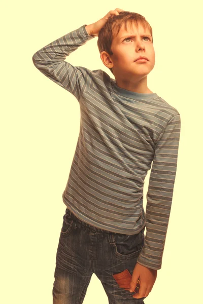 Blond kid boy in a striped sweater thinks scratching his head ha — Stock Photo, Image