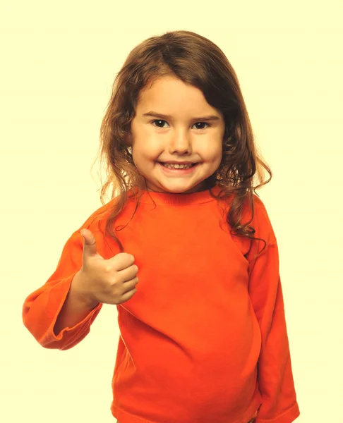 Little brunette curly girl in an orange jacket, showing thumbs u — Stock Photo, Image