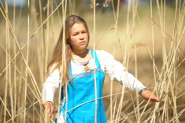 Menina em um vestido azul em um campo de grama seca alta — Fotografia de Stock