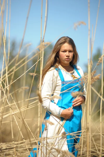 Menina em um vestido azul em um campo de grama seca alta — Fotografia de Stock