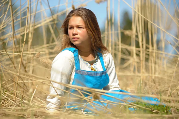 Menina em um vestido azul em um campo de grama seca alta — Fotografia de Stock