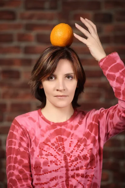 Portrait of young woman holding orange on her head — Stock Photo, Image