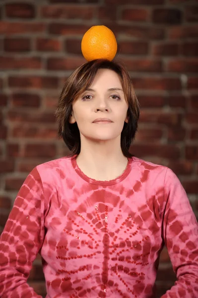 Portrait of young woman holding orange on her head — Stock Photo, Image