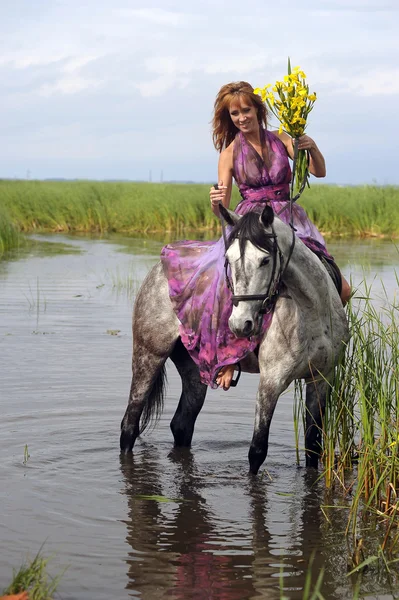 Jonge vrouw in een jurk op een paard in water — Stockfoto