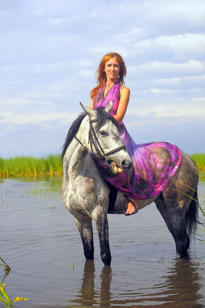 Jeune femme en robe sur un cheval dans l'eau — Photo