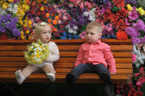 Děti na lavičce s květinami v pozadí — Stock fotografie