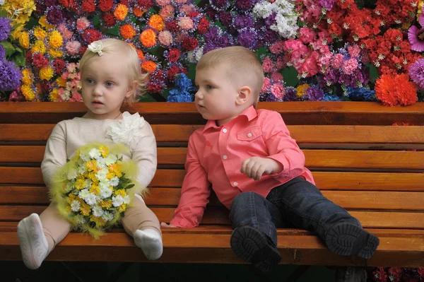 バック グラウンドで花とベンチ上の子供 — ストック写真