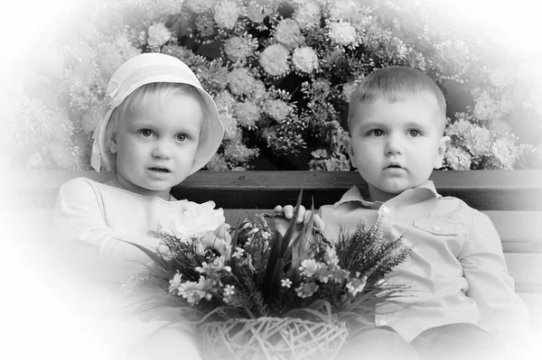 Děti na lavičce s květinami v pozadí — Stock fotografie