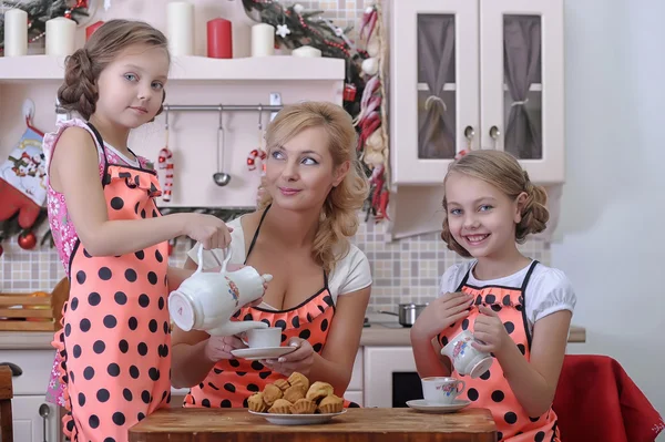 Mãe com suas filhas na cozinha bebendo chá com cupcakes — Fotografia de Stock