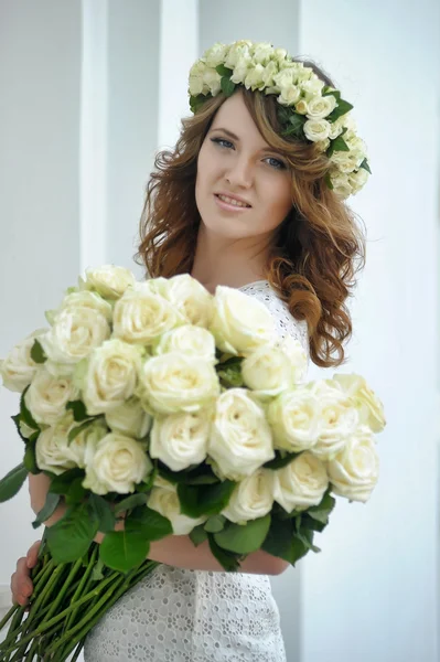 Retrato de uma mulher bonita com um buquê de rosas brancas e uma coroa de flores na cabeça — Fotografia de Stock