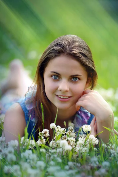 Usmívající se nedospělý dívka vleže na pozadí zelený jetel — Stock fotografie