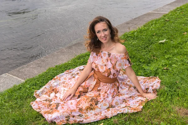 Pembe Elbiseli Güzel Esmer Kadın Nehir Kenarındaki Çimlerin Üzerinde Oturuyor — Stok fotoğraf