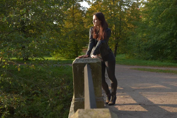 秋の公園で黒の革のジャケットと黒のジーンズのブルネットの女の子 — ストック写真
