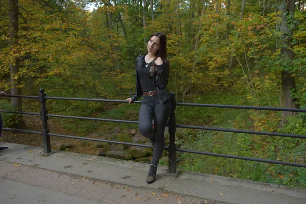 秋の公園で黒の革のジャケットと黒のジーンズのブルネットの女の子 — ストック写真