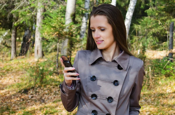 La mujer hermosa con el teléfono móvil a pie en la madera —  Fotos de Stock