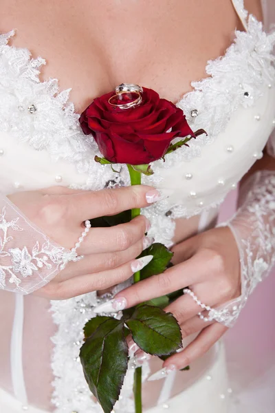 La novia sostiene en una mano una rosa roja con anillos de boda . —  Fotos de Stock