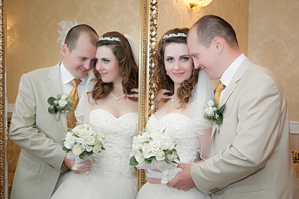 Groom and the bride stand near a mirror with a gold frame Stock Photo