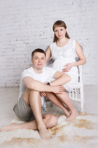 Marido se sienta en un piso y la esposa embarazada se sienta al lado en una silla — Foto de Stock